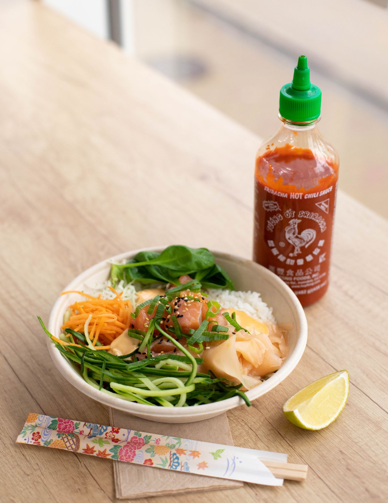 Huy Fong rooster brand sriracha hot chili sauce bottle beside a salmon poke bowl