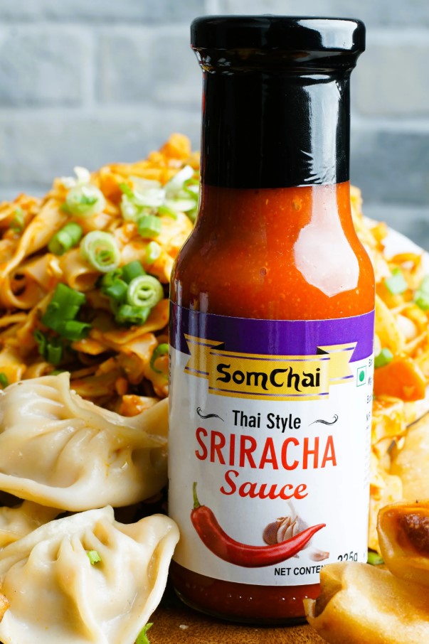 Bottle of Thai style sriracha hot chili sauce served beside fried dumplings and noodles