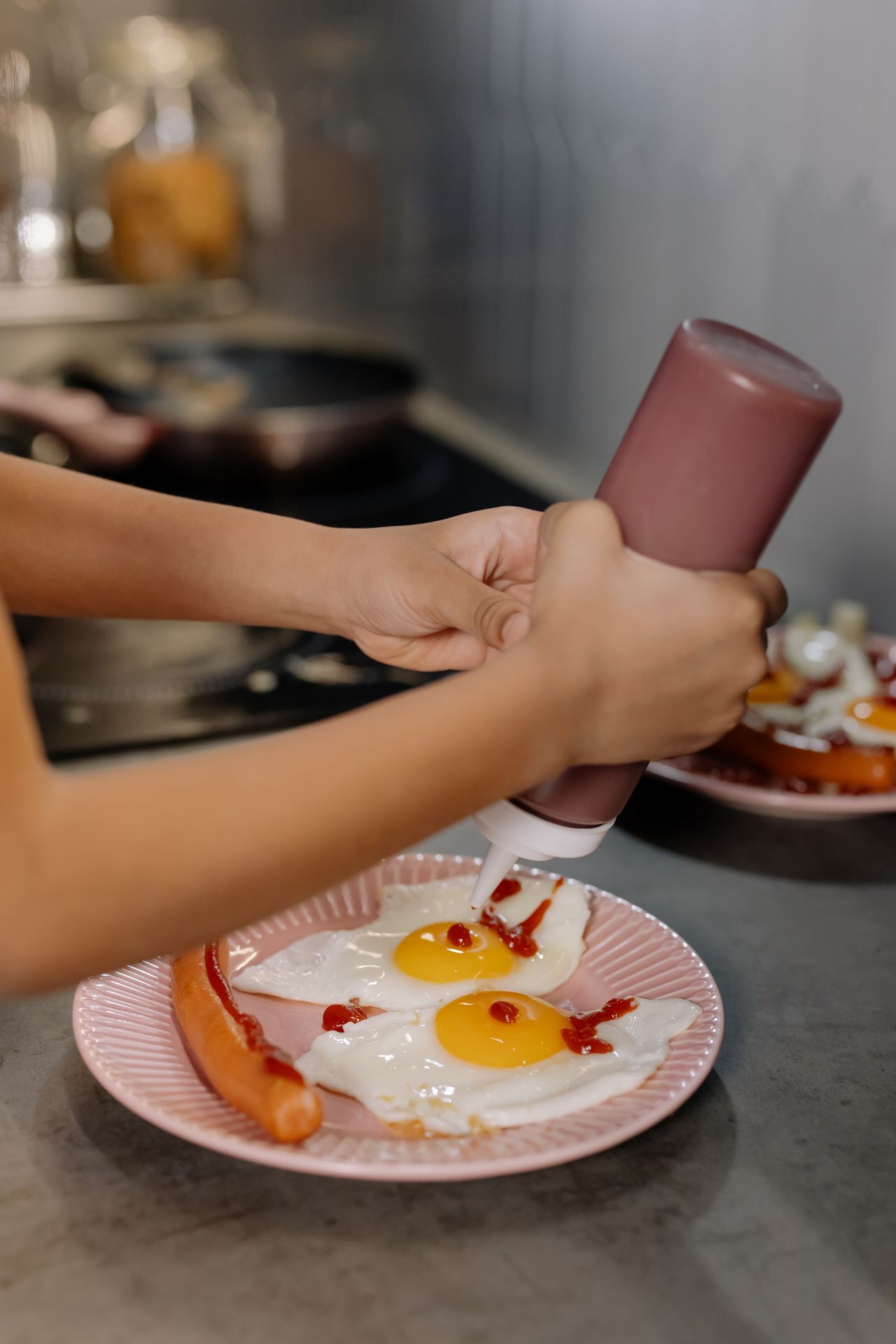 Hand squeezing sriracha hot chili sauce onto fried eggs and a sausage on a plate