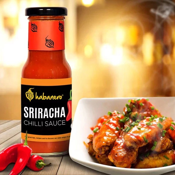 Bottle of sriracha chilli sauce with fresh red chilies and a plate of chicken wings