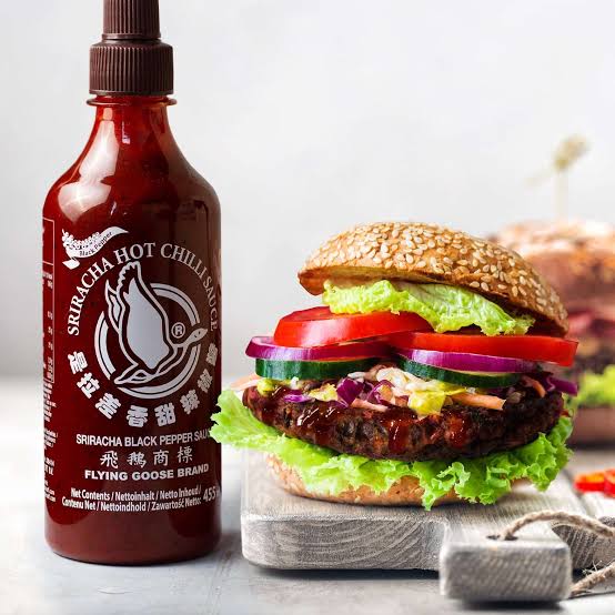 Bottle of sriracha hot chili sauce with a sesame seed burger showing finished product quality